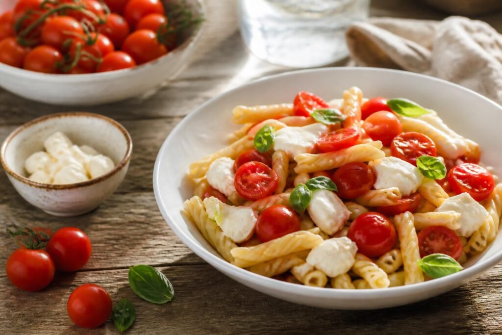 Pasta estiva con pomodorini di Pachino IGP, basilico fresco e olio extravergine degli Iblei su tavolo di legno rustico